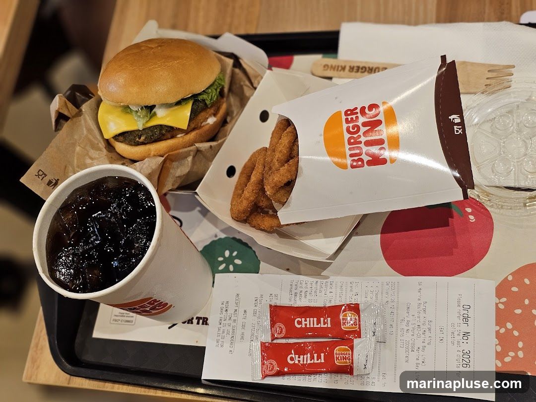 A Burger King meal consisting of a burger, onion rings, a cup of soda, and two packets of chili sauce, laid out on a tray with a receipt.