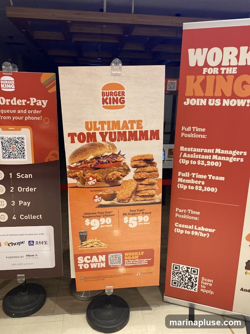 Three promotional banners for Burger King are displayed. The leftmost banner advertises an "Order-Pay" system via phone with QR codes. The central banner features the "ULTIMATE TOM YUMMMM" promotion, showcasing a burger and chicken nuggets, with prices for the Ultimate Tom Yum Tendercrisp Chicken meal and Tom Yum BK Nuggets meal. It also includes a "SCAN TO WIN" weekly draw for a Thai-riffle Songkran & Bach Thaid Laguna Singapore Staycation. The rightmost banner is a recruitment advertisement titled "WORK FOR THE KING," detailing full-time and part-time positions with salary ranges.
