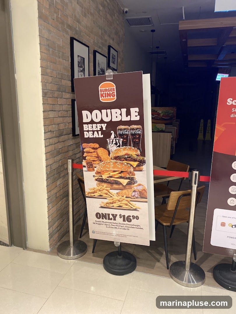 A promotional sign for Burger King's Double Beefy Deal, featuring images of burgers, fries, chicken nuggets, and drinks. The deal is priced at $16.90 and includes a Double Mushroom Swiss, Double Cheeseburger, BK Nuggets (6pcs), Taro Pie (1 pc), Chocolate Sundae, 2x Fries (M), and 2x Coke (S).