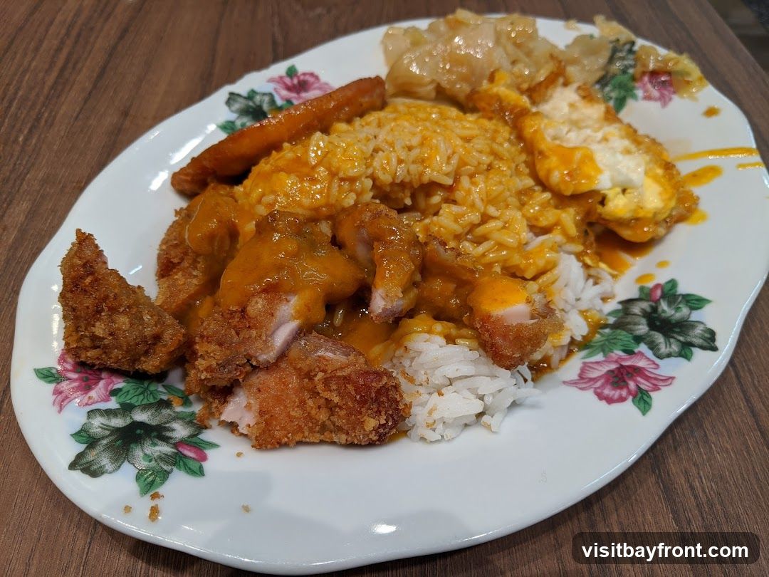 A plate of white rice topped with curry sauce, pieces of fried chicken, a fried egg, and a sausage. The plate has a floral pattern around the rim.