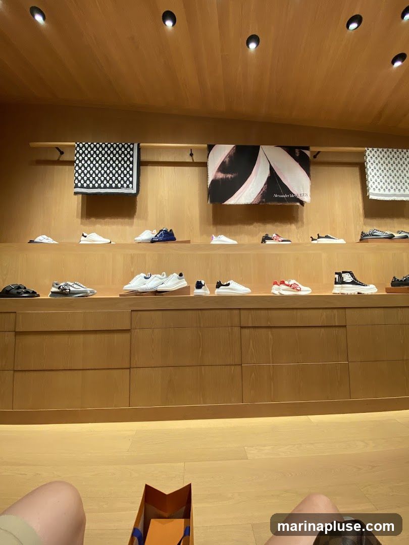A well-lit interior of a store with wooden walls and shelves displaying various sneakers and scarves. The shelves are organized with shoes in neat rows, and decorative scarves are hung above. In the foreground, a shopping bag is visible on the floor, and a person's legs are in view.