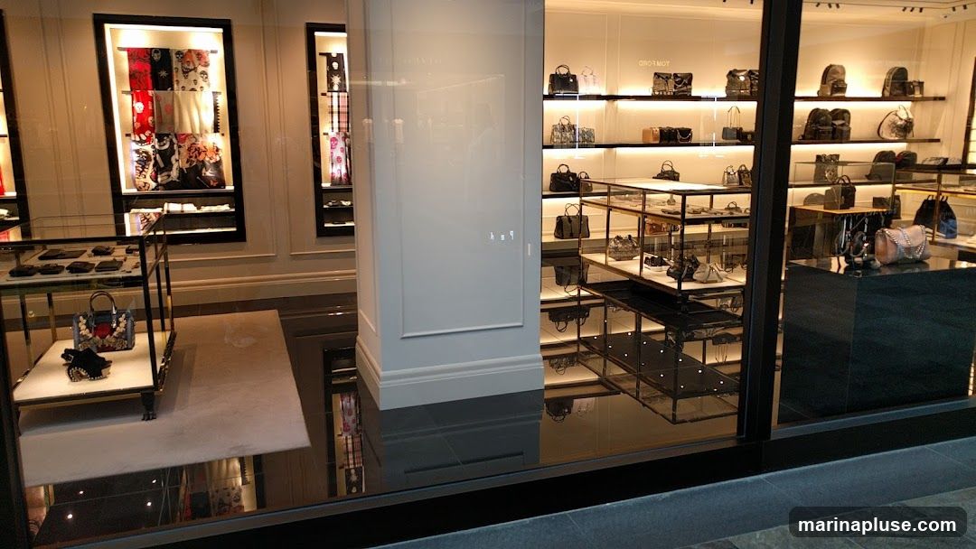 A well-lit store interior displays a variety of luxury handbags, backpacks, wallets, and scarves. The merchandise is neatly arranged on shelves and display cases, with spotlights highlighting individual items. The store features a modern and elegant aesthetic, with polished floors and clean lines.