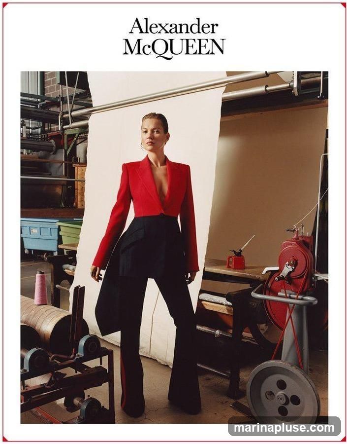 A fashion editorial image featuring a model wearing a red blazer and black flared trousers. The background appears to be a workshop or studio setting with industrial machinery, spools of thread, and fabric. The Alexander McQueen logo is visible at the top of the image.