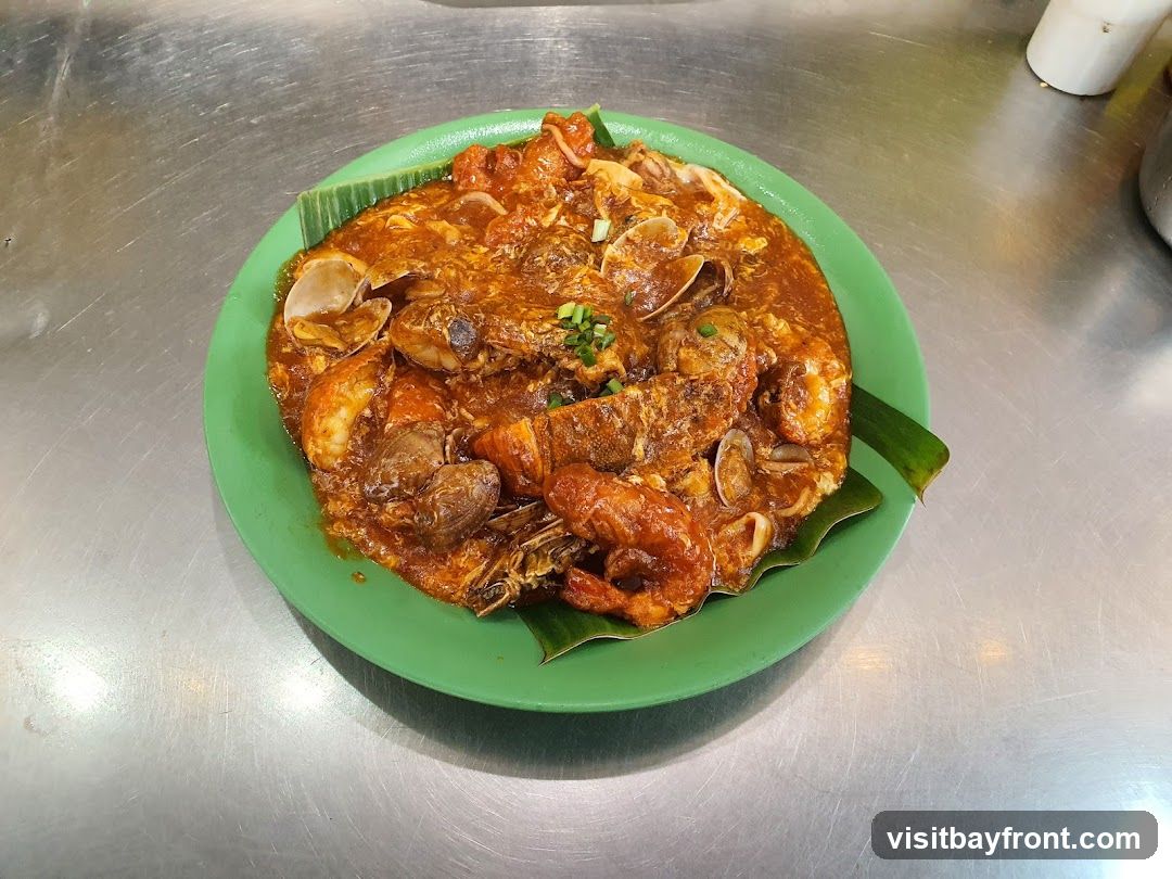 A green plate filled with a seafood stir-fry dish, featuring prawns, clams, and other seafood in a rich, orange-red sauce. The dish is garnished with banana leaves and served on a metallic surface.
