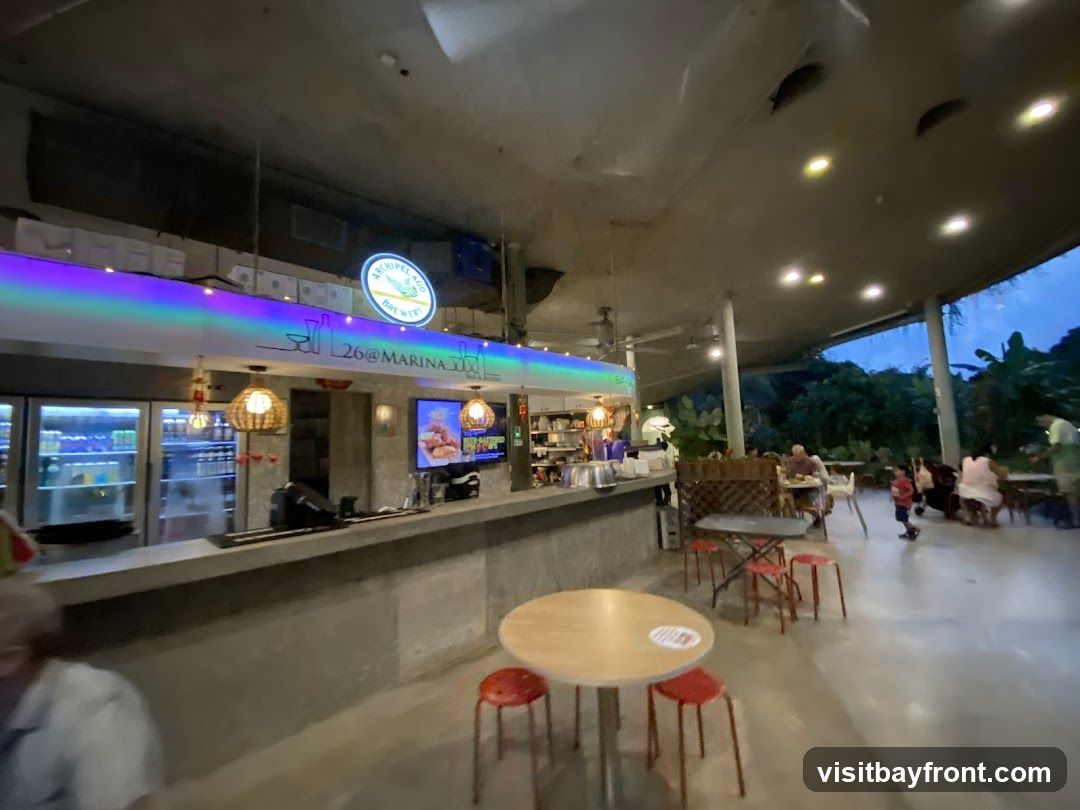 An interior view of a bar and restaurant with a long counter, refrigerators stocked with drinks, and seating areas. A sign above the counter reads "26@MARINA" and a circular logo for "ARCHIPELAGO BREWERY" is visible. People are seated at tables in the background.