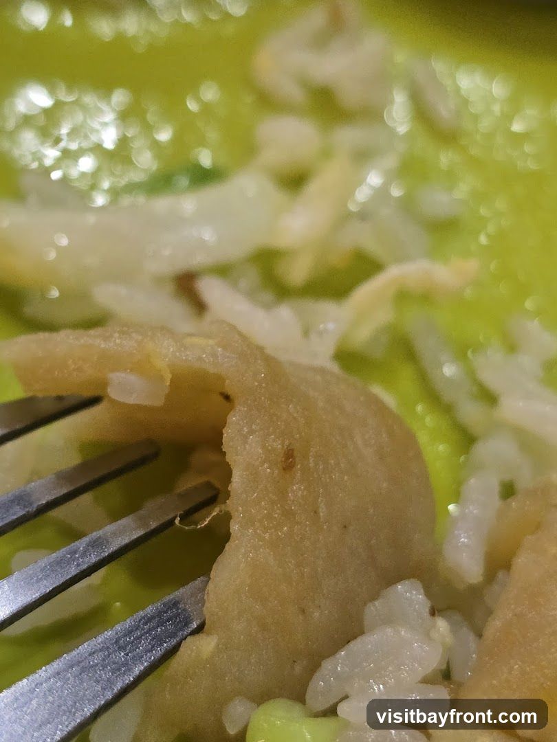 A close-up shot of a fried dumpling being picked up by a fork, served with white rice and green peas on a bright green plate. The dumpling appears golden brown and slightly crispy, with visible rice grains inside. The lighting creates soft bokeh effects in the background.