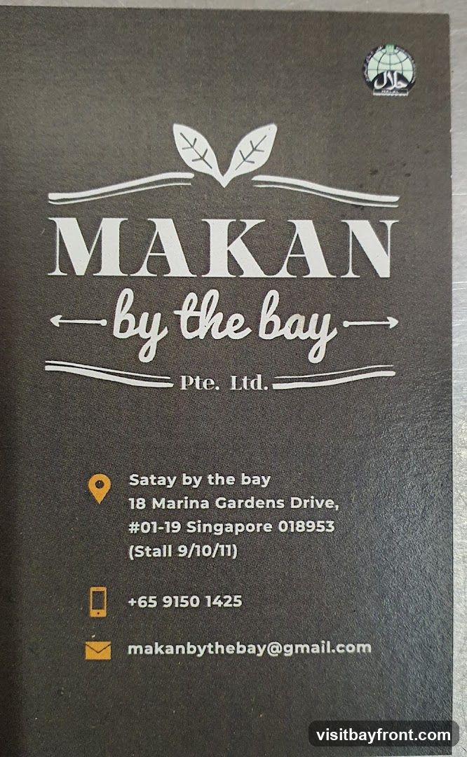 A business card for Makan by the bay Pte. Ltd. It features the company name in large white font, with a stylized leaf logo above it. Below the name, it says "by the bay" in a script font. The card also includes contact information: the address is "Satay by the bay, 18 Marina Gardens Drive, #01-19 Singapore 018953 (Stall 9/10/11)". The phone number is "+65 9150 1425" and the email address is "makanbythebay@gmail.com". A Halal certification logo is visible in the top right corner.