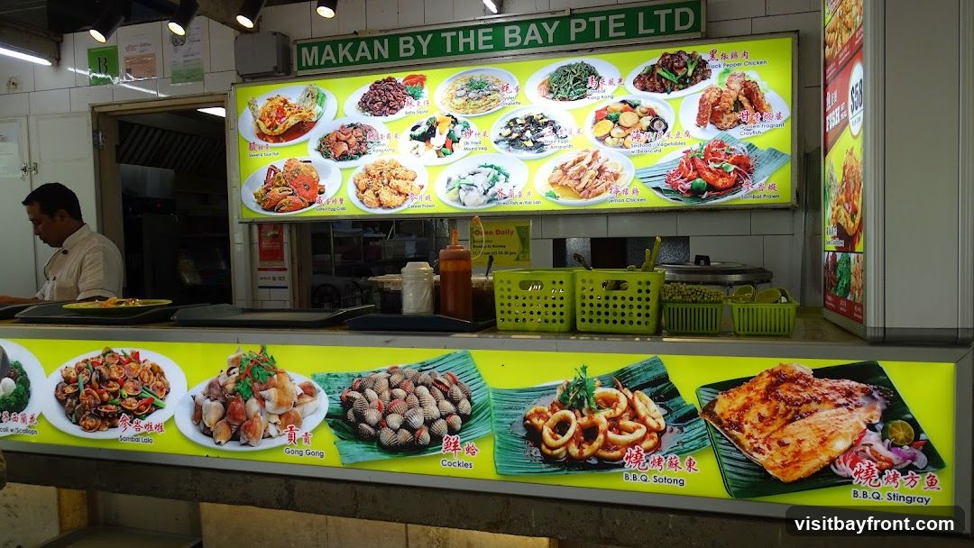 A food stall with a large illuminated menu board displaying various dishes. A chef is visible in the background. The menu features images and names of seafood and other dishes.
