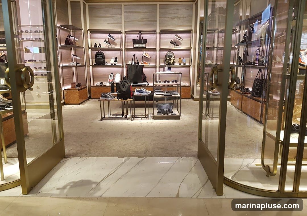 A view into a high-end store displaying shoes, handbags, and sunglasses on shelves and display stands. The store features a clean, modern aesthetic with marble flooring and plush carpeting. The merchandise is neatly arranged, highlighting the brand's collection.