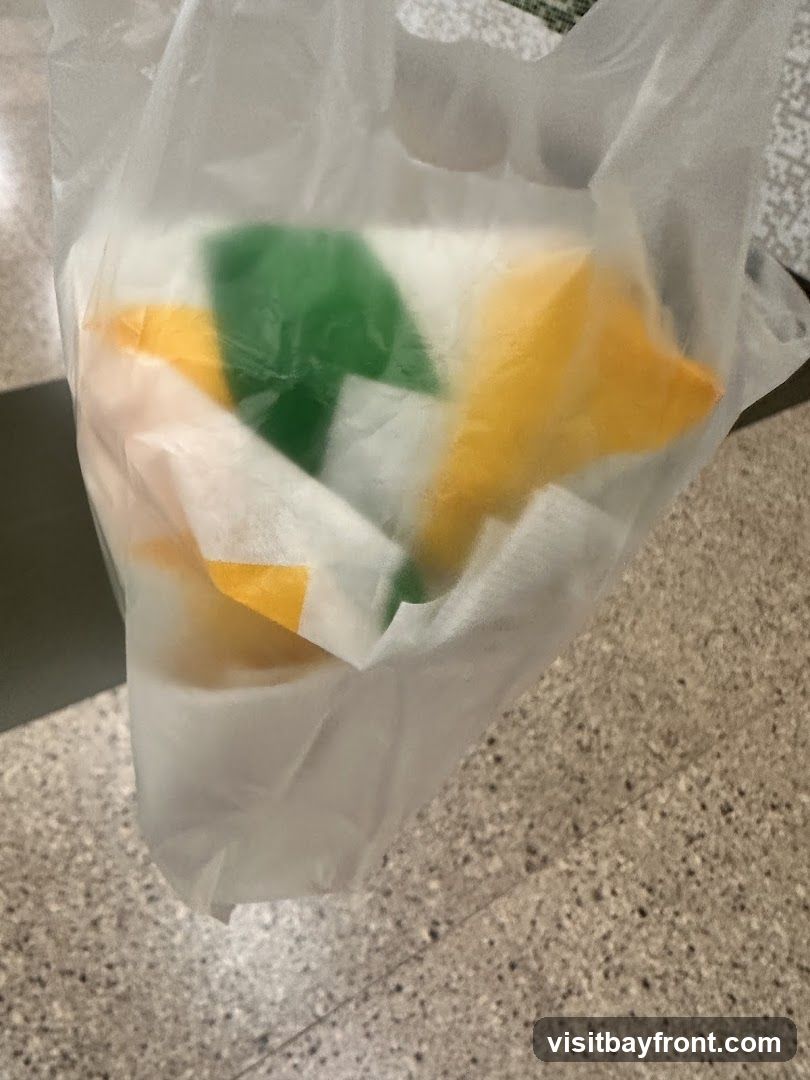 A white plastic bag containing food items. The food items are wrapped in paper with the Subway logo colors of green and yellow visible. The bag is resting on a speckled floor.