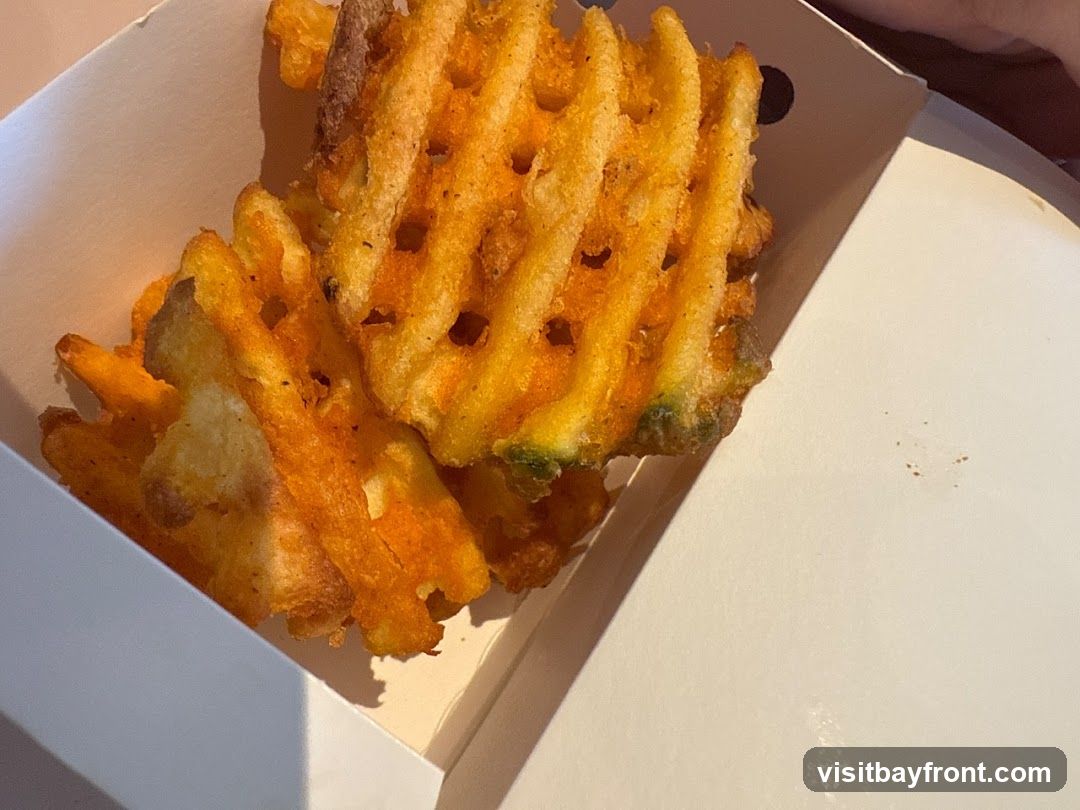 A close-up shot of golden-brown waffle fries in a white paper container. The fries appear crispy and seasoned.