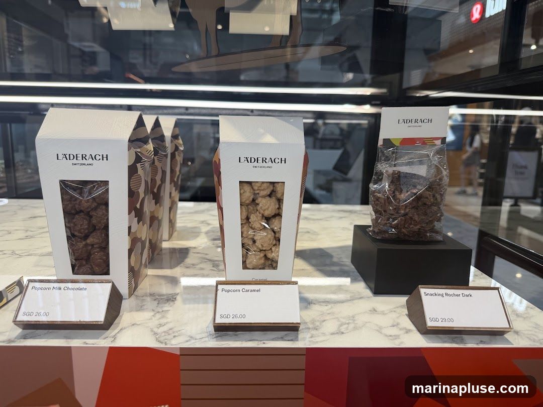 A display of Läderach chocolates and popcorn treats in packaging and bags. The products are arranged on a marble-like surface with price tags.