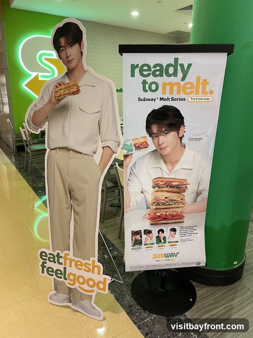A cutout of a man holding a sandwich stands next to a promotional banner for Subway's Melt Series. The banner features the same man and text that reads "ready to melt." Below the man's image on the banner are smaller images of him and text related to a photocard giveaway with the Subway Melt Series combo. The Subway logo is visible in the background.