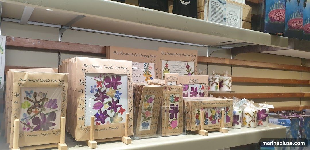 A display of various handmade items featuring real pressed orchids, including note books, hanging boards, and bookmarks. Candles with floral designs are also visible.