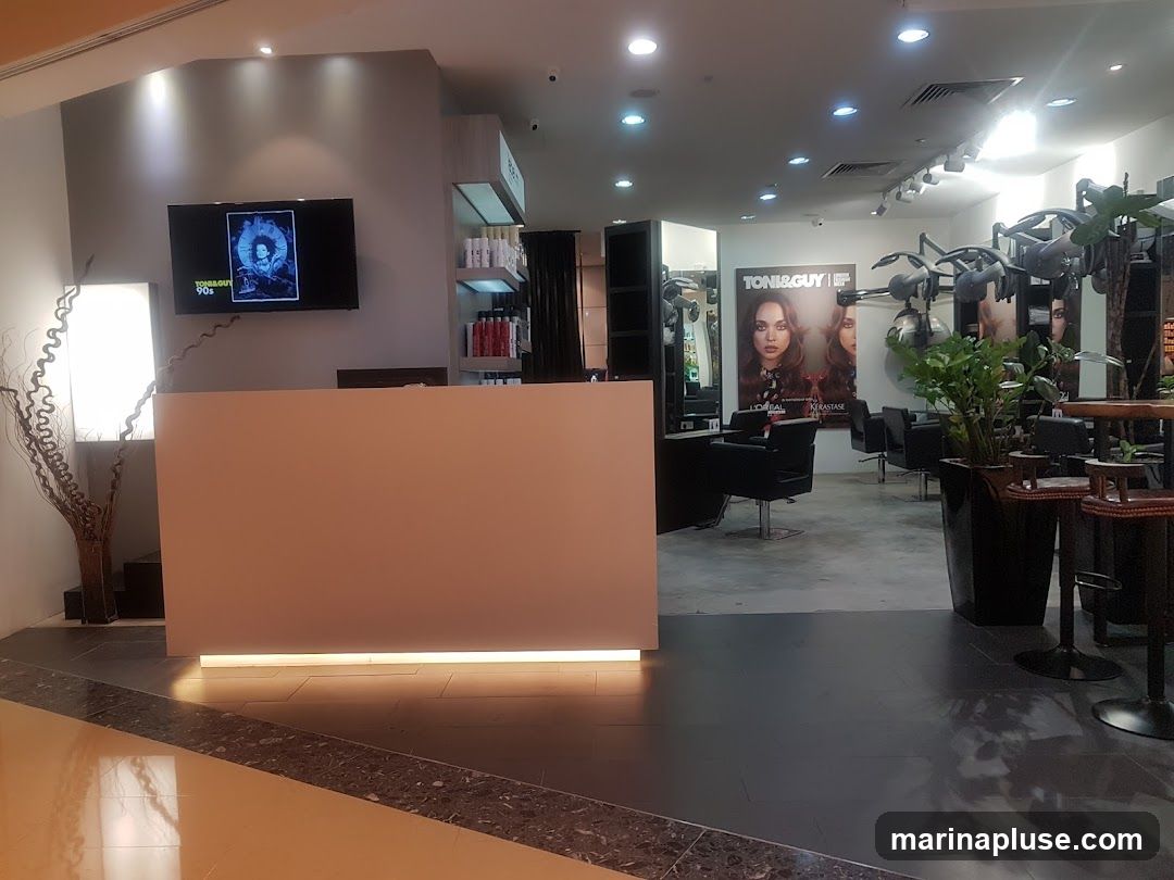 The interior of a hair salon with a reception desk, styling chairs, and product shelves. A large poster for TONI&GUY is visible on the wall.