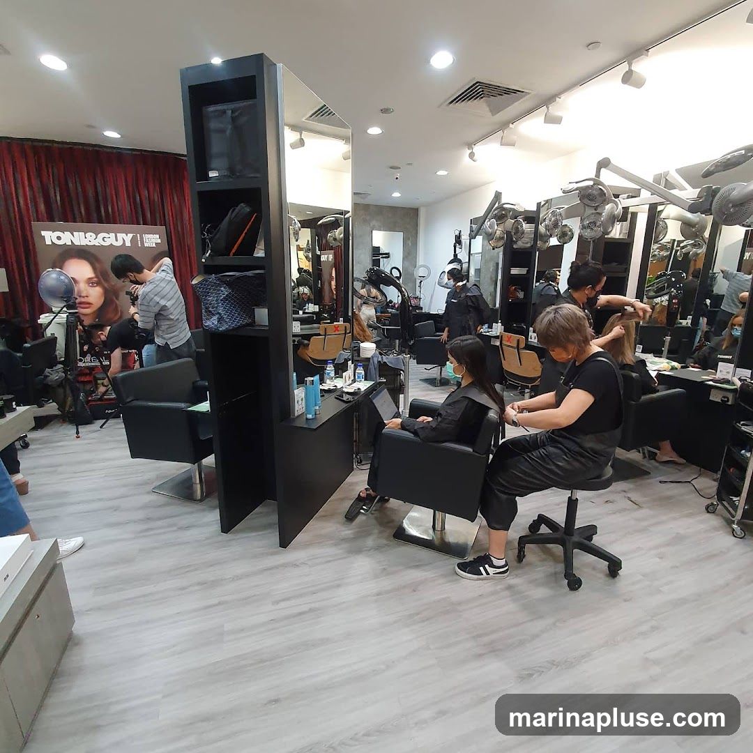 A busy hair salon with multiple stylists attending to clients. There are several styling stations, mirrors, and hair dryers. A large poster for TONI&GUY is visible on the left wall.