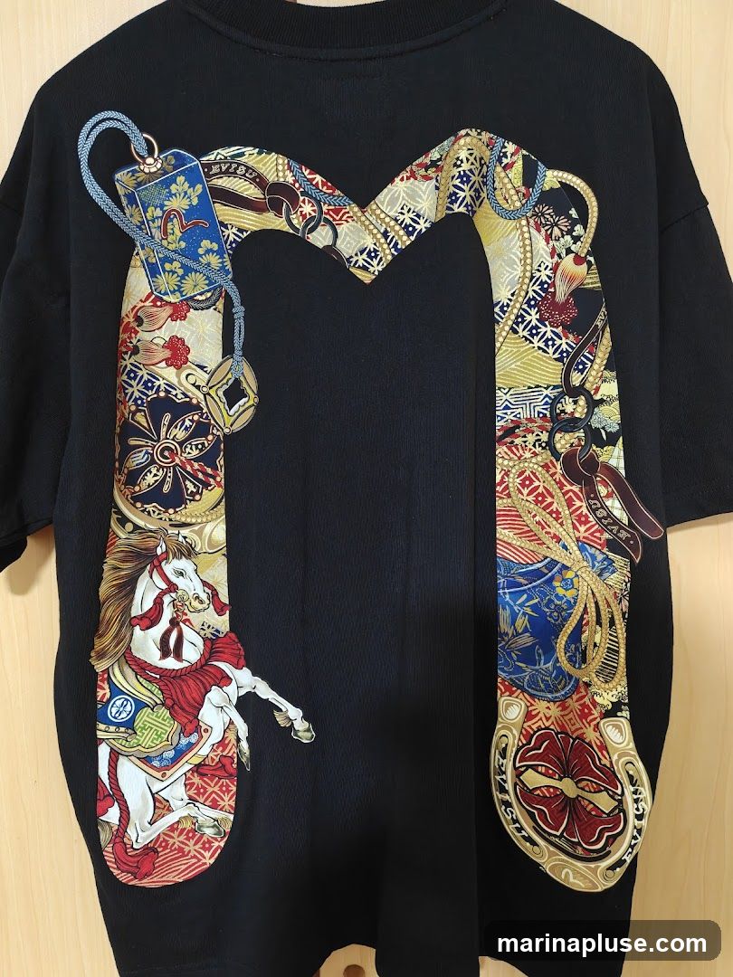 A black t-shirt with a large, colorful graphic design. The design features a white horse with red and gold accents, appearing to be on a carousel. Surrounding the horse and extending across the chest is an ornate, ribbon-like pattern with various motifs including buckles, ropes, and traditional Japanese-inspired prints in shades of blue, red, gold, and white. The brand name "EVISU" is visible within the design.