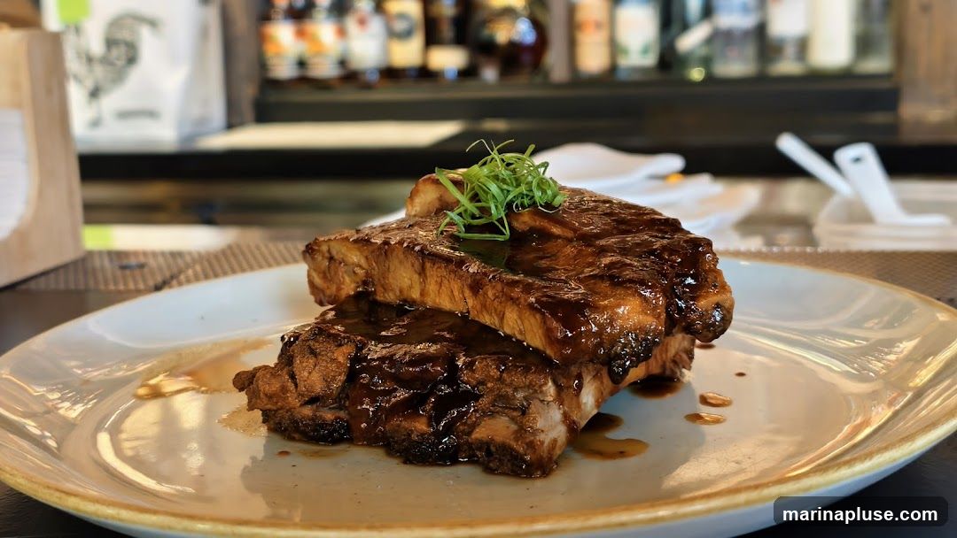 A plate of BBQ ribs glazed with a dark sauce and garnished with green onions. The ribs are stacked on top of each other on a light-colored plate. In the background, bottles of liquor are visible on shelves behind a bar.