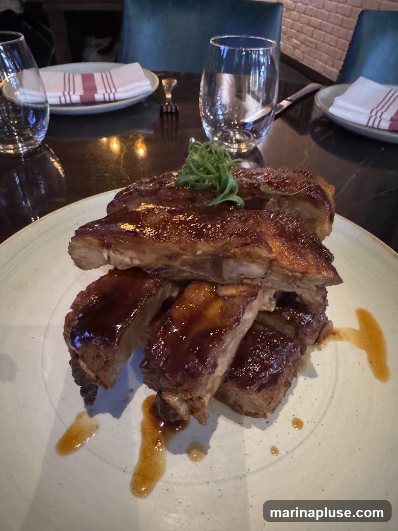 A plate of glazed ribs is presented on a table setting with wine glasses and napkins.