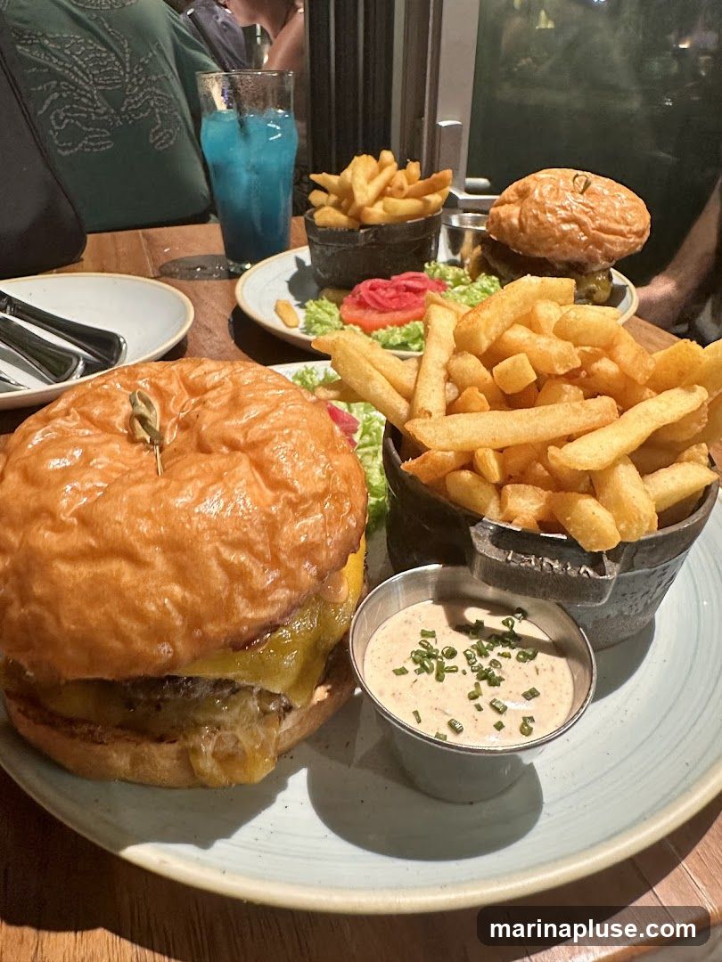 A close-up shot of two burgers with fries and dipping sauce on a table. A blue drink is visible in the background.