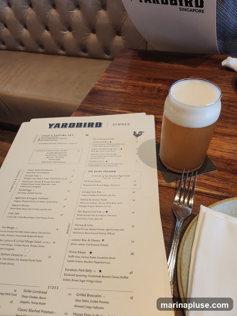 A menu from Yardbird Singapore with sections for Specials, Starters & Shares, Mains, and Sides. A glass of beer and a fork are on the table.
