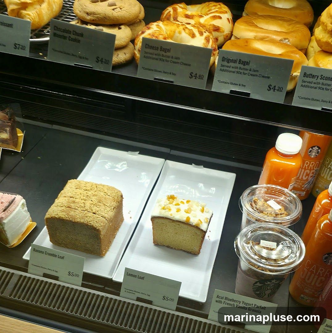 A display case filled with various pastries, including croissants, cookies, bagels, loaves of bread, and parfaits. Several bottles of juice and cups with yogurt parfaits are also visible.