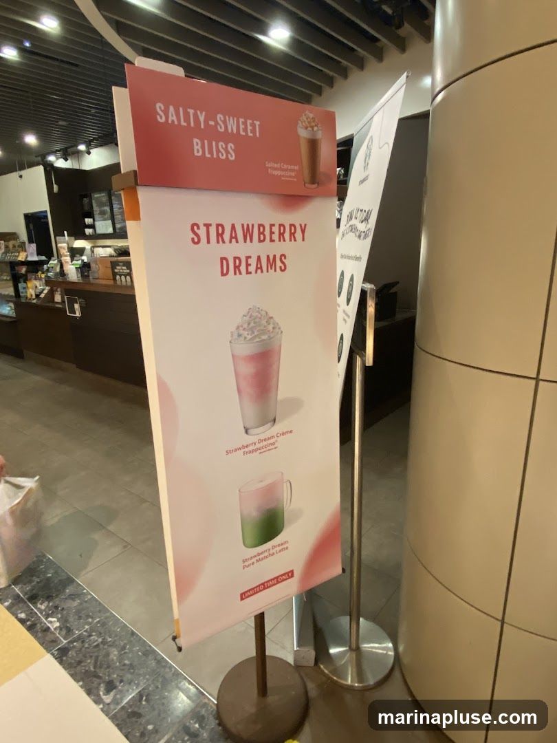 A promotional sign displays two drinks: a Salted Caramel Frappuccino at the top, and below it, "Strawberry Dreams" featuring a Strawberry Dream Crème Frappuccino and a Strawberry Dream Pure Matcha Latte. The sign indicates that the Strawberry Dream drinks are a limited-time offer. In the background, a counter with a menu board and a Starbucks logo is visible.