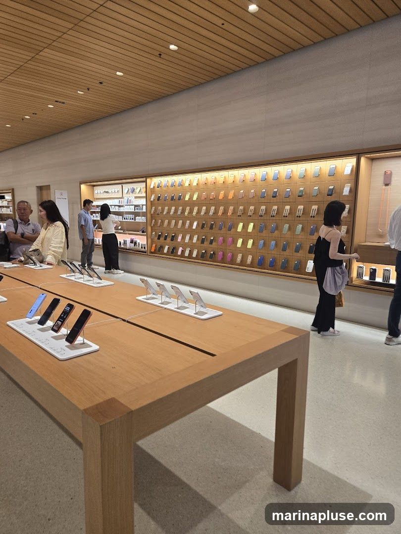 An interior view of an Apple Store, showcasing a large display wall filled with various phone cases. In the foreground, a wooden table displays several iPhones on stands. Customers are browsing the merchandise.