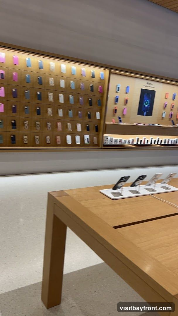 A retail store interior with a wall display of numerous iPhone cases in various colors. Below the case display, a section shows iPhones on stands. A wooden table is in the foreground, also displaying iPhones on stands.