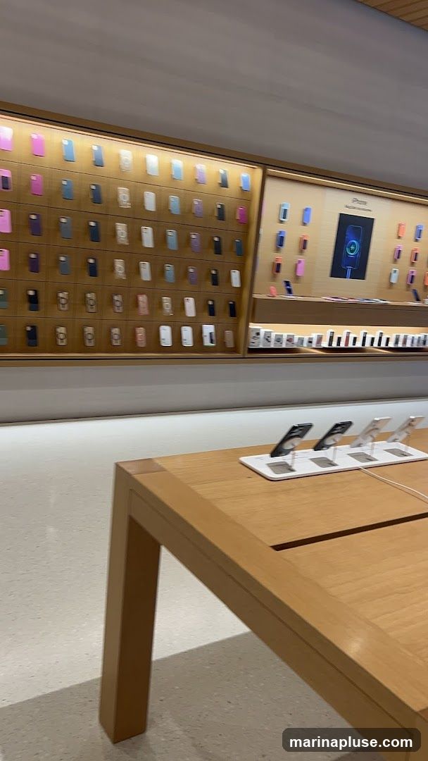 A retail store interior with a wall display of numerous iPhone cases in various colors. Below the case display, a section shows iPhones on stands. A wooden table is in the foreground, also displaying iPhones on stands.