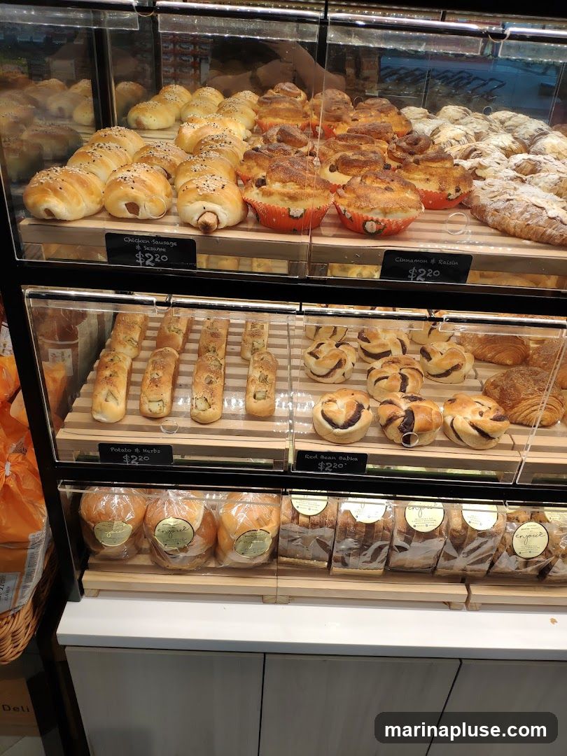 A display case filled with various baked goods, including sausage rolls, sweet buns, bread loaves, and pastries. Some items have price labels.