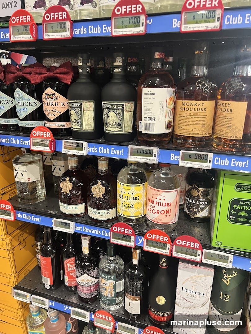 A retail display of various bottles of alcohol, including gin, whiskey, and cognac, on multiple shelves. Several bottles are marked with "OFFER" tags and prices.