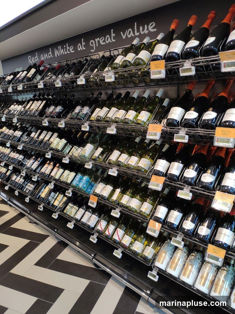 A retail display of numerous bottles of wine, both red and white, arranged on shelves. A sign above reads "Red and White at great value." Several bottles have "Special Offer" tags with prices visible. The flooring is a black and white herringbone pattern.