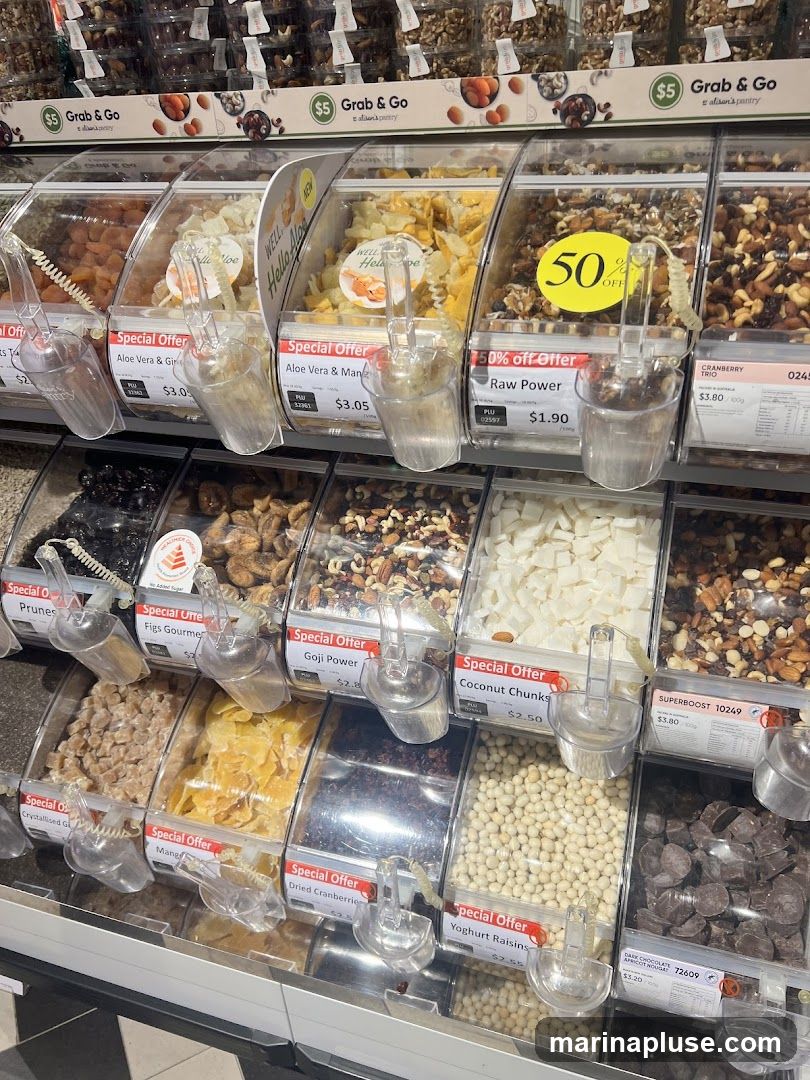 A display of various bulk food items in clear bins, including dried fruits, nuts, and candies. Many bins have special offer labels and price tags.