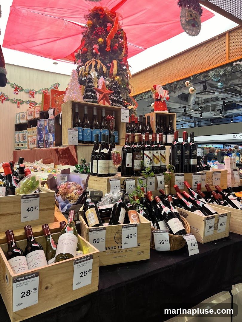 A festive display of wine bottles arranged in wooden crates, with a decorated Christmas tree and Santa Claus figures in the background. Various bottles of red and white wine are prominently featured, with price tags indicating different selections. The display appears to be set up in a retail environment, possibly a supermarket or liquor store, during the holiday season.
