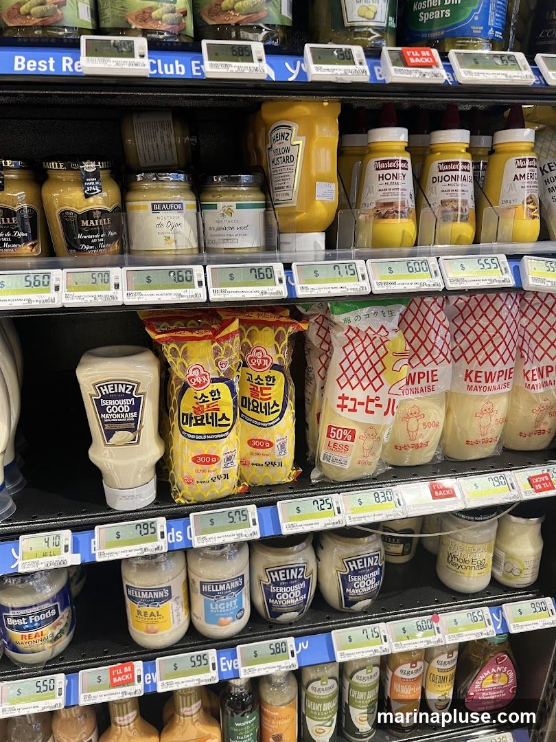 A shelf in a store displaying various brands and types of mustard, mayonnaise, and other condiments. Brands visible include Heinz, Maille, Beaufor, Masterfood, Best Foods, Hellmann's, Kewpie, and Newman's Own. Prices are displayed on electronic shelf labels.
