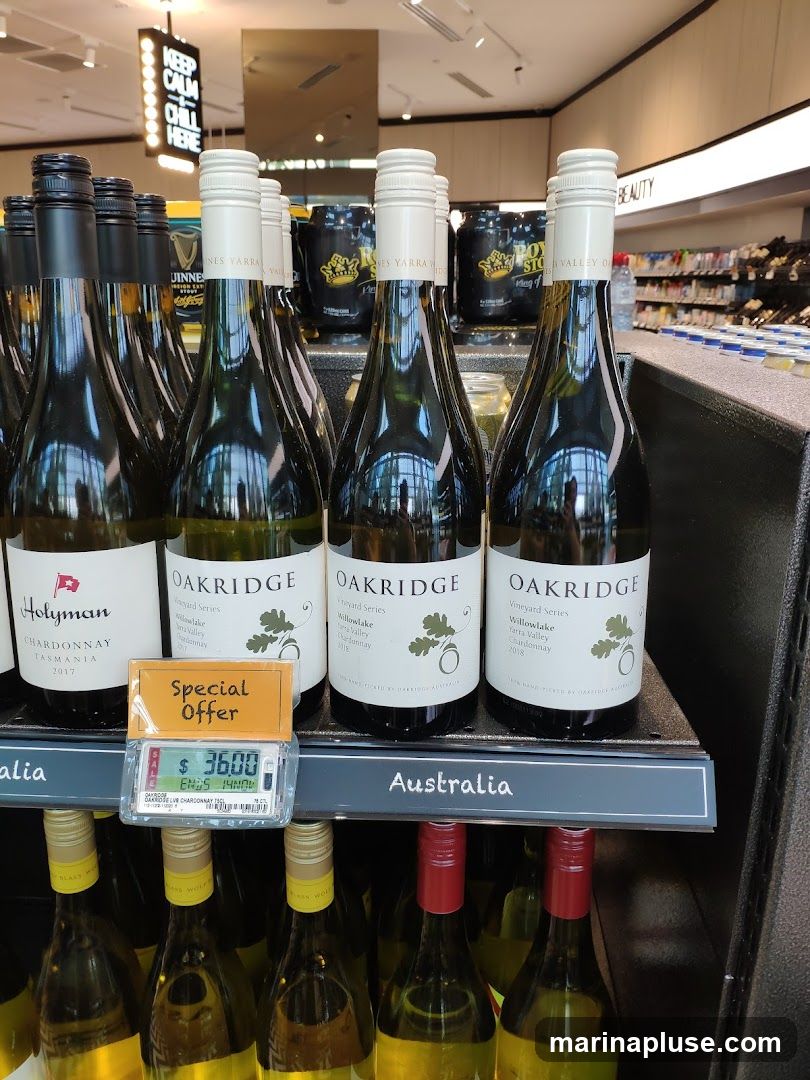 A selection of wine bottles are displayed on shelves in a retail environment. The bottles in the foreground are labeled 'Holyman Chardonnay Tasmania 2017' and 'Oakridge Vineyard Series Willowlake Yarra Valley Chardonnay'. A 'Special Offer' sign is visible with a price of $36.00. In the background, other bottles and shelves stocked with various products can be seen.