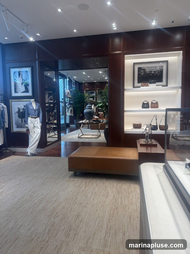 The image shows the interior of a high-end retail store, likely a clothing boutique or department store. The decor is sophisticated, with dark wood paneling, warm lighting, and plush carpeting. Mannequins are dressed in elegant attire, and shelves display handbags and framed artwork. A large, ornate vase sits on a table in the background, adding to the luxurious ambiance. The overall impression is one of refined taste and exclusivity.