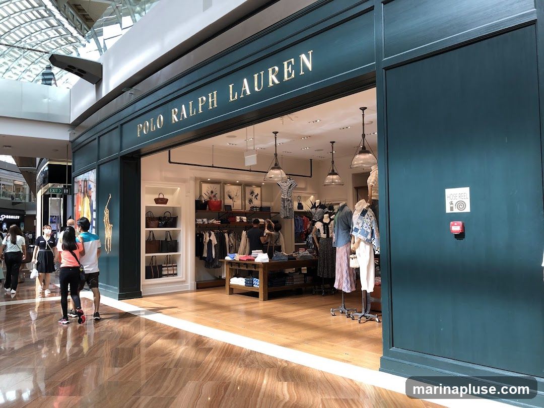 The exterior of a Polo Ralph Lauren store with the brand name visible above the entrance. Inside, clothing and accessories are displayed on shelves and racks. Several mannequins showcase outfits. People are walking by the store entrance.