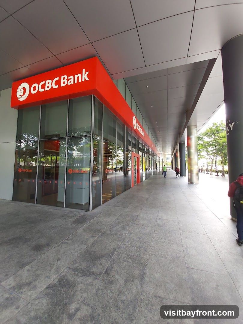 The exterior of an OCBC Bank branch with large glass windows and prominent orange signage displaying the bank's name and logo. The building is modern with a covered walkway.