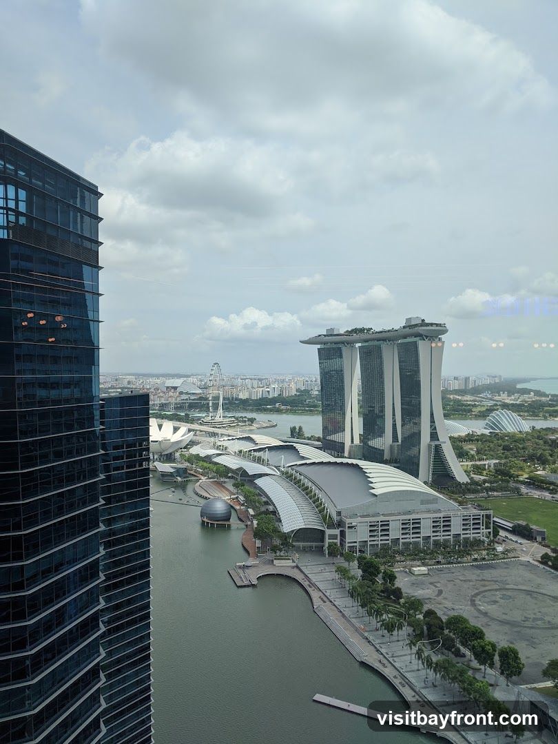 A panoramic view of the Singapore skyline on a cloudy day, featuring the Marina Bay Sands hotel, the ArtScience Museum, and other modern architecture. The image is taken from a high vantage point, looking out over a body of water and a bustling cityscape.