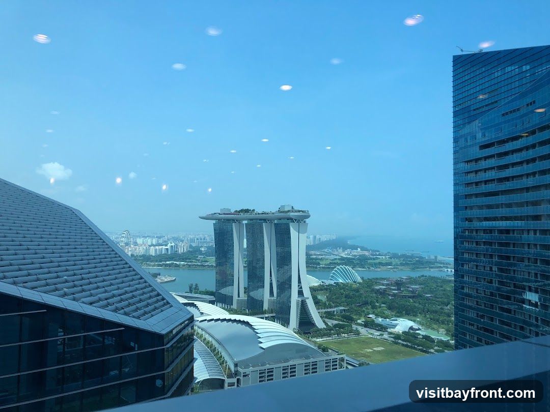 A panoramic view of a city skyline, featuring modern skyscrapers and a distinctive hotel with a boat-shaped structure on top. The scene is bathed in daylight under a clear blue sky with scattered reflections on the glass.