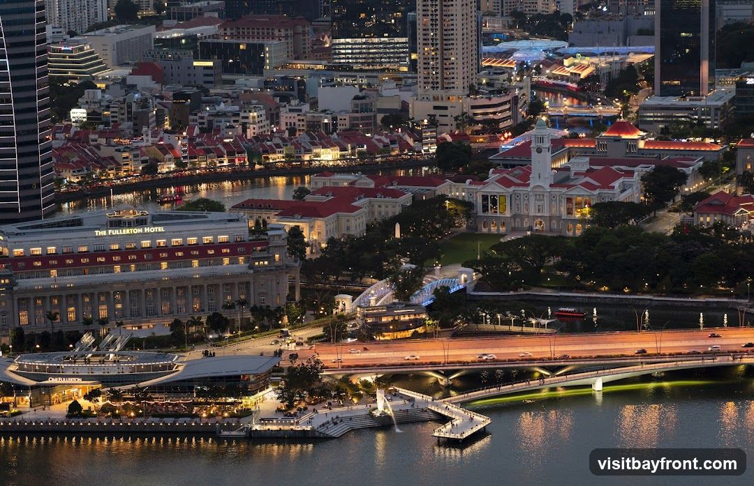 An aerial view of a city skyline at dusk, with a river flowing through it. The Fullerton Hotel is prominently visible, along with other buildings and bridges illuminated by lights. The scene captures the vibrant atmosphere of the city at night.