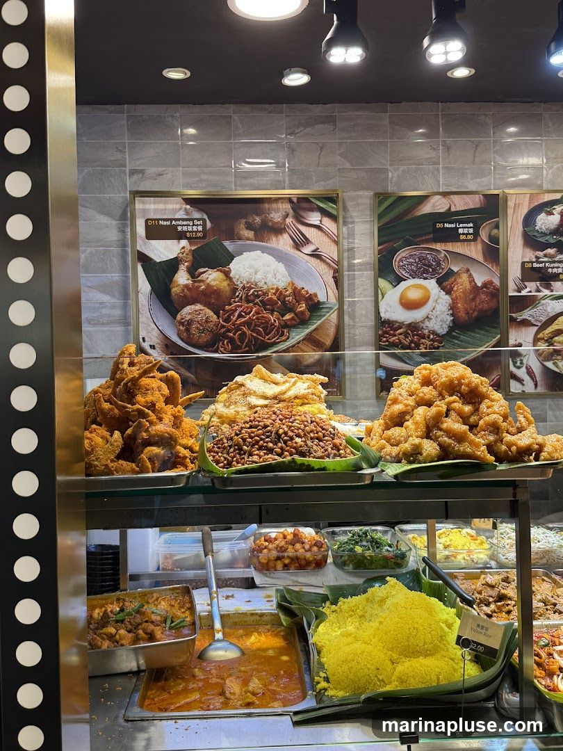 A display of various food items, including fried chicken, rice dishes, curries, and side dishes. There are also framed pictures of menu items on the wall.