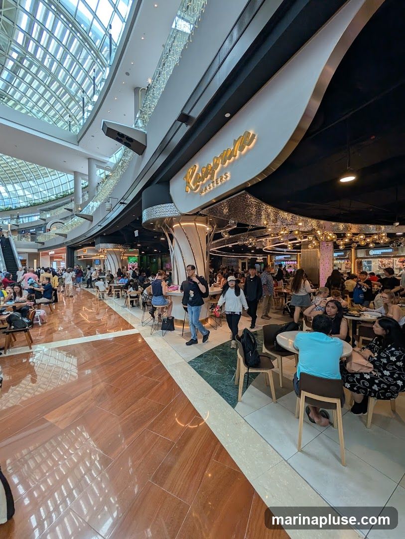 A bustling food court with many people dining and walking. The signage for "Ramen Masters" is visible above the entrance to a restaurant. The floor is made of polished wood and marble tiles.