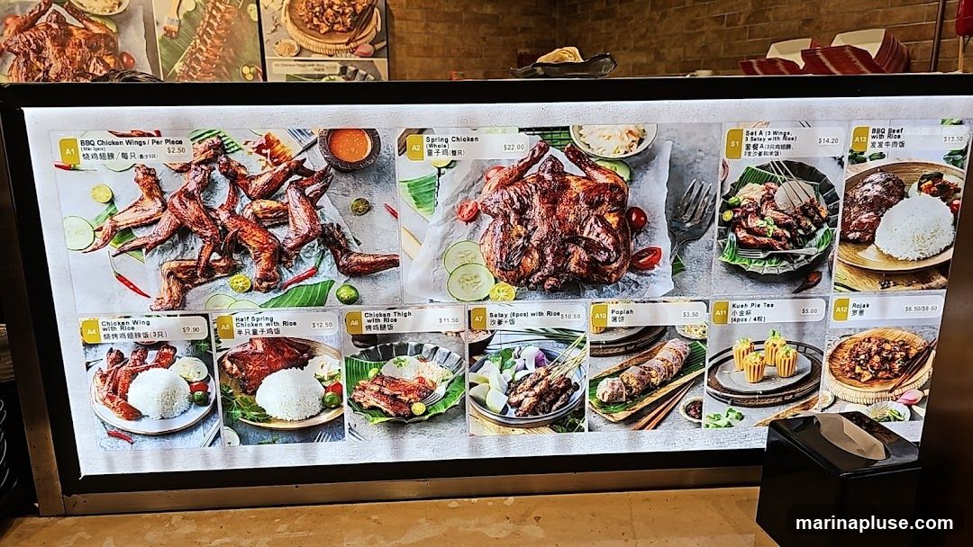 A digital menu board displaying various chicken dishes, satay, beef rice, and other items with prices.