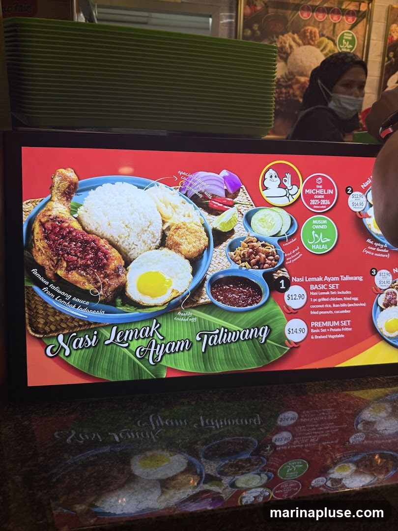 A digital menu board displaying Nasi Lemak Ayam Taliwang dishes. It features images of the food and lists prices and descriptions. The menu includes Michelin Guide and Halal certifications.