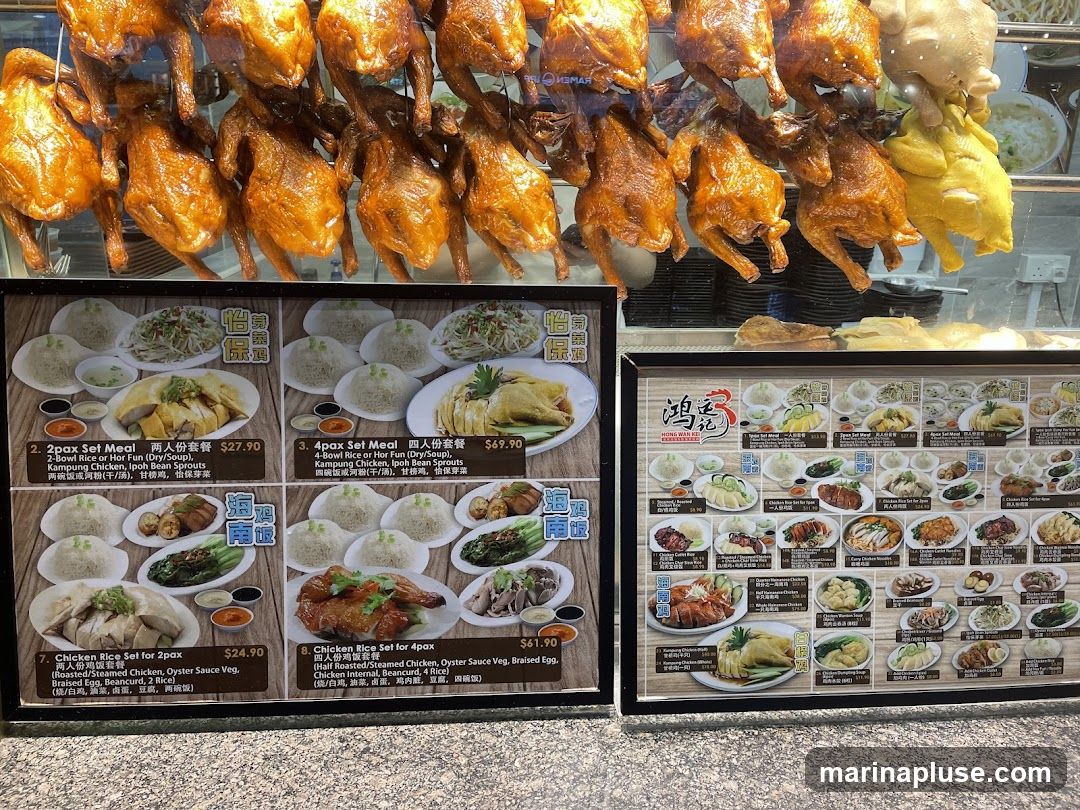 A display of several whole roasted chickens hanging in a food establishment, with two menu boards below. The menu boards show various set meals featuring chicken and rice or noodles, with prices and descriptions.