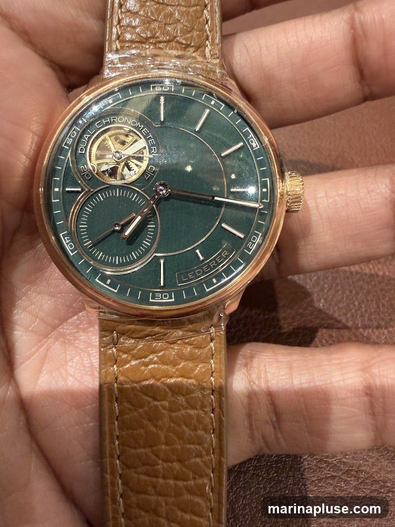 A close-up shot of a man's wrist wearing a rose gold watch with a green dial. The watch has a tourbillon visible at the 10 o'clock position and a sub-dial at the 6 o'clock position. The watch band is made of brown leather. The brand name "LEDEFER" is visible on the dial.