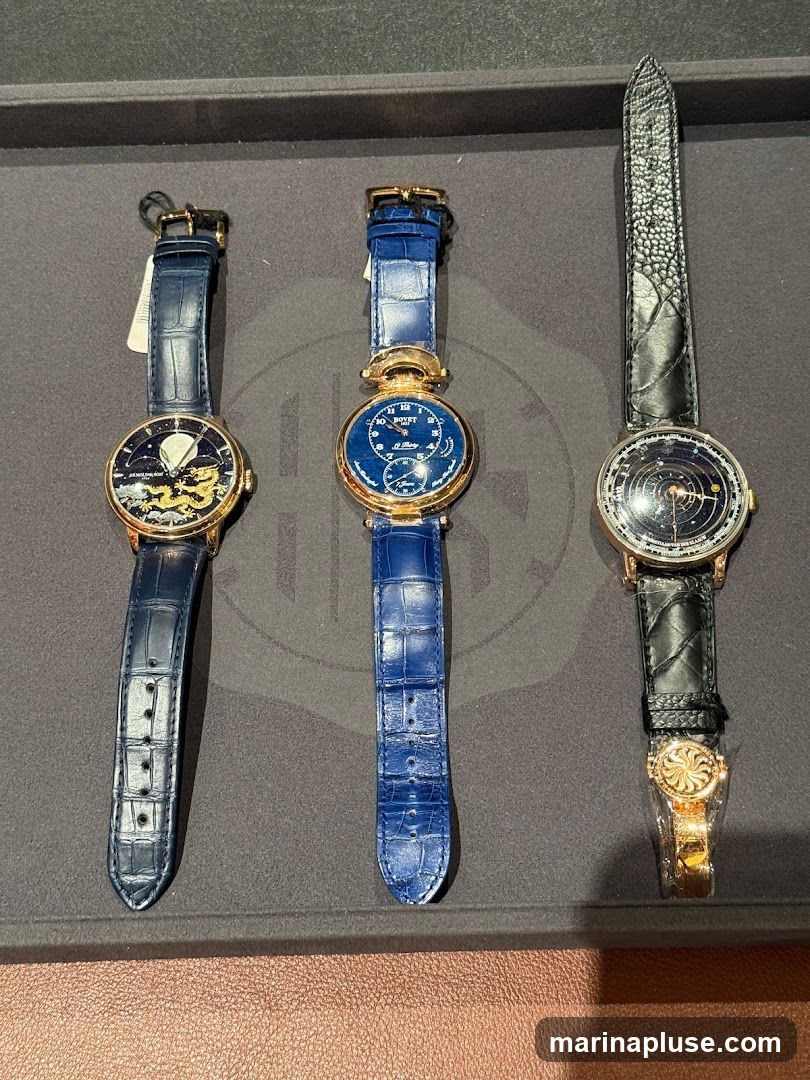 Three luxury watches are displayed on a dark gray surface. The watch on the left has a dark blue alligator strap and a gold case. Its dial features a celestial scene with a moon and golden dragons. The middle watch also has a dark blue alligator strap and a gold case. Its dial is blue with white text and markings, and the brand name "BOVET" is visible. The watch on the right has a black textured strap and a gold case. Its dial is dark with a celestial map or diagram. The watches appear to be new, with some protective plastic still attached to the watch on the right.